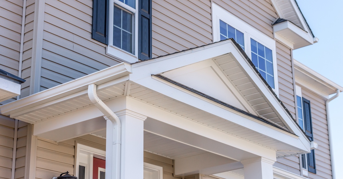 A close-up of the entrance of a vinyl-sided home, with a roof structure supported by white rectangular columns.