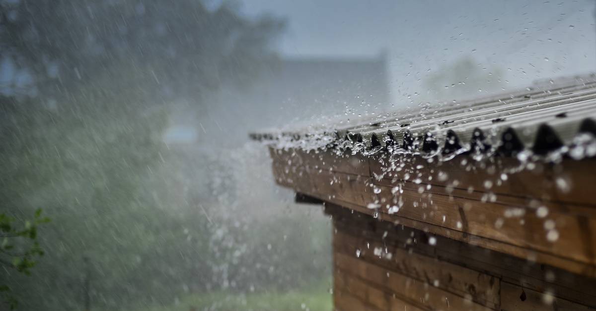 Rain bouncing and flowing off of a black-colored metal roof. Trees and gray skies fill the background.