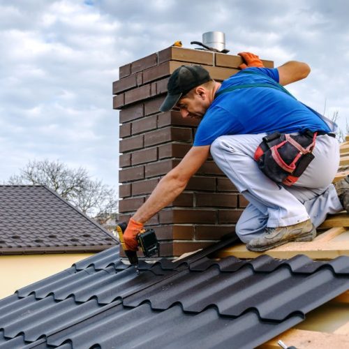 A close-up of a professional roofer covering a roof with black Mediterranean-style roofing shingles.